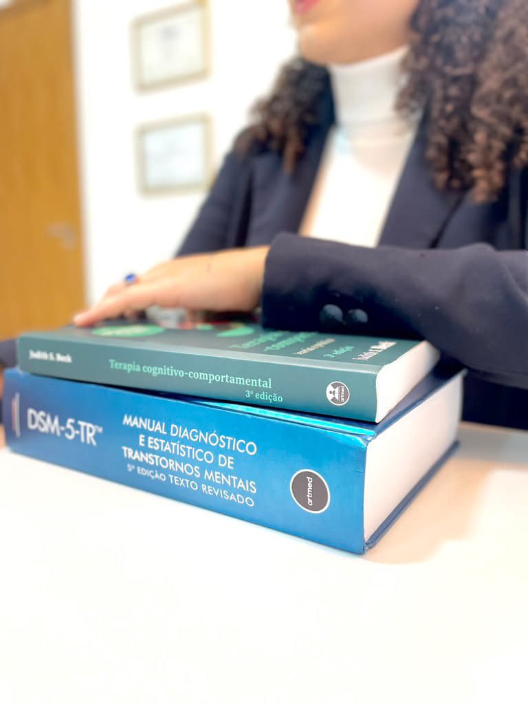 Mão de Bruna Ribeiro sobre os livros Terapia Cognitivo-Comportamental, de Judith Beck, e o DSM-5-TR